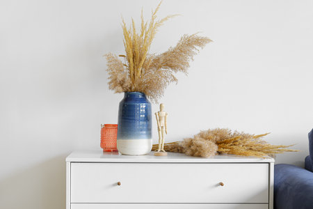Vase with bouquet of beautiful dried flowers on chest of drawers near light wallの写真素材