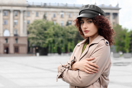 Portrait of young woman in leather cap holding her shoulders on city squareの写真素材