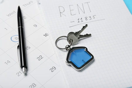 Calendar, note pad with word RENT, pen and keys with house shaped keychain, closeup