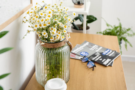 Vase with chamomiles on table near light wallの写真素材