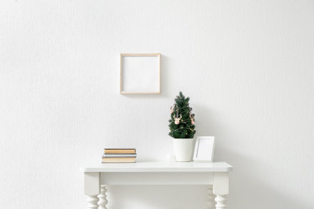 Small Christmas tree, frame and books on table near light wallの写真素材