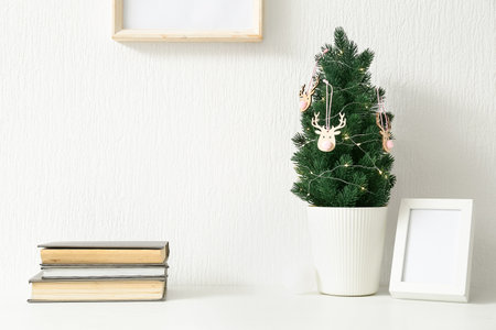 Small Christmas tree, frame and books on table near light wallの写真素材
