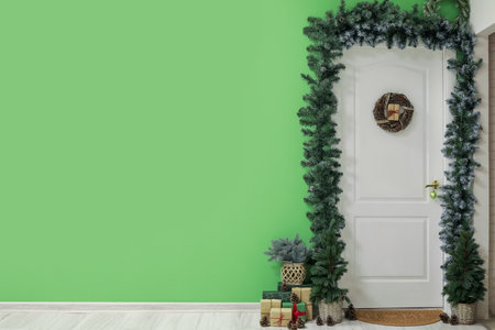 White door with Christmas wreath, fir trees, branches and presents in hallの写真素材