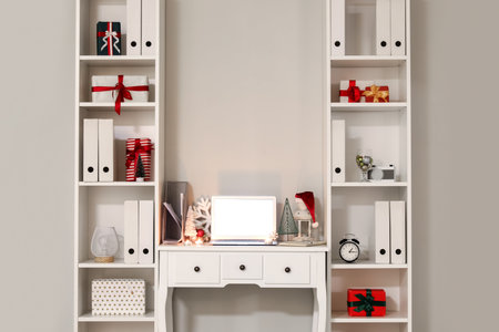 Workplace with laptop, Santa hat, candles and Christmas decor in light officeの写真素材