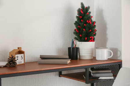 Workplace with small Christmas tree and calendar near light wallの写真素材