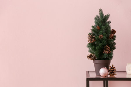 Small Christmas tree with fir cones and ball on table near pink wallの写真素材