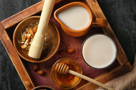 Wooden board with jug, glass of almond milk, nuts and honey on dark background, closeupの写真素材