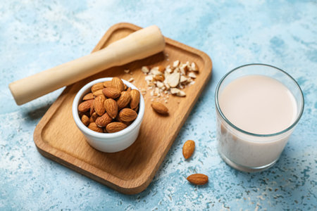Glass of almond milk, wooden board with nuts and masher on color backgroundの写真素材