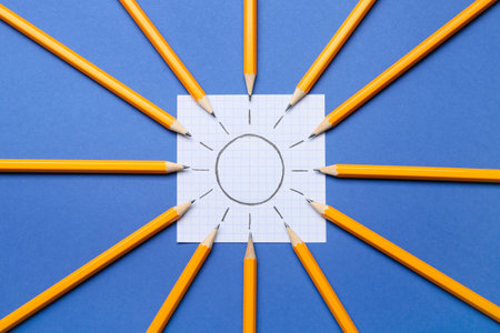 Composition with ordinary pencils and sheet of paper with drawn sun on blue background, closeupの写真素材