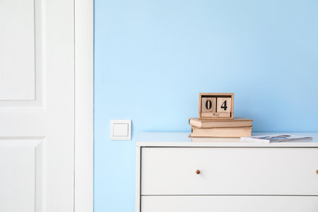Calendar with books on chest of drawers near blue wall