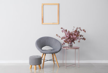 Vase with blossoming branches on table and armchair near light wallの写真素材