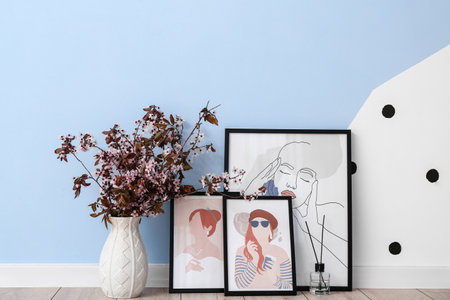 Vase with blossoming branches and pictures on floor near color wall