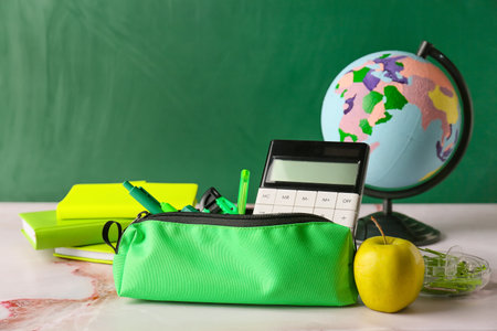 Pencil case with stationery, globe and apple on table in classroomの写真素材