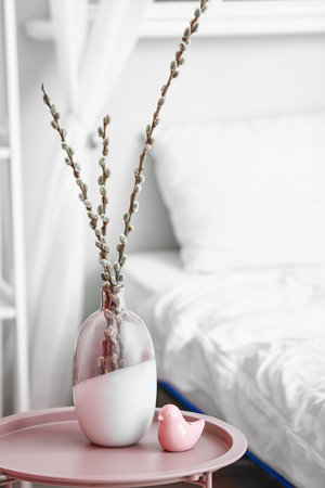 Vase with willow branches on table near bed in roomの写真素材