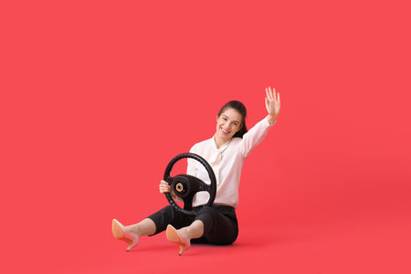 Young businesswoman with steering wheel waving hand on color backgroundの写真素材