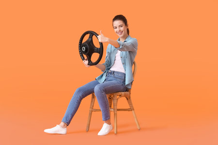 Young woman with steering wheel showing thumb-up on color background