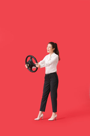 Young businesswoman with steering wheel on red background