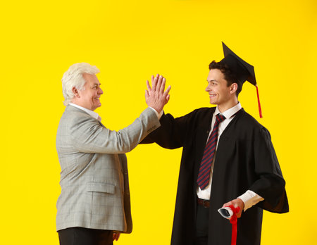 Happy male graduation student with his father on color backgroundの写真素材