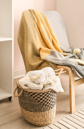 Basket with knitting yarn, needles and clothes in the room