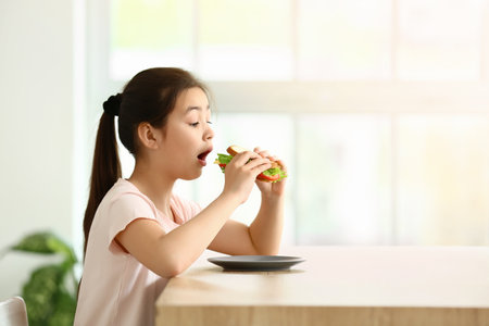Little girl eating tasty sandwich in the kitchenの写真素材