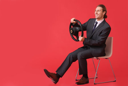 Young businessman with steering wheel sitting on chair against color backgroundの写真素材