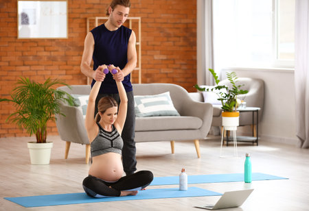Young pregnant woman and her husband practicing yoga at homeの写真素材