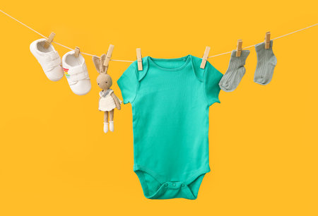 Baby clothes, shoes and toy hanging on rope against color backgroundの写真素材