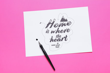 Paper with text HOME IS WHERE THE HEART IS and nib pen on pink backgroundの写真素材