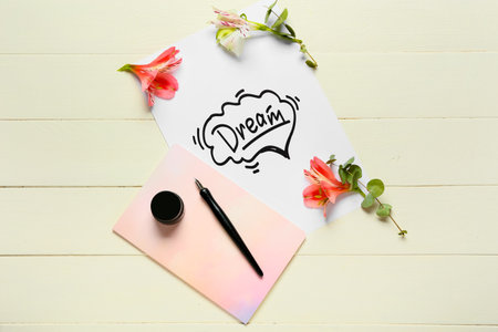 Paper with word DREAM, flowers, notebook and ink on white wooden backgroundの写真素材