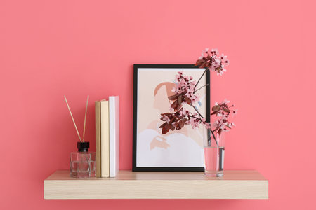 Book shelf with blossoming branches and picture hanging on color wall
