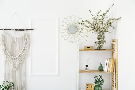 Vase with blossoming branches on shelf near light wall