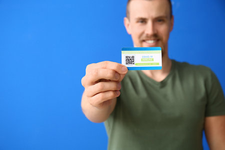 Young man with vaccination card on color background, closeup