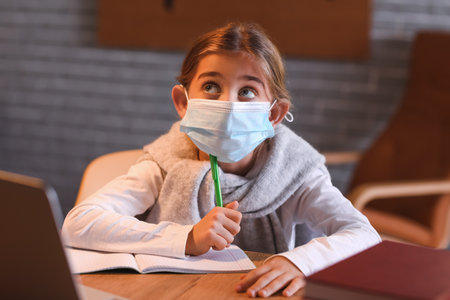 Little girl in medical mask studying online at home in the eveningの写真素材