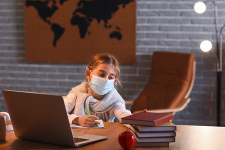 Little girl in medical mask studying online at home in the eveningの写真素材