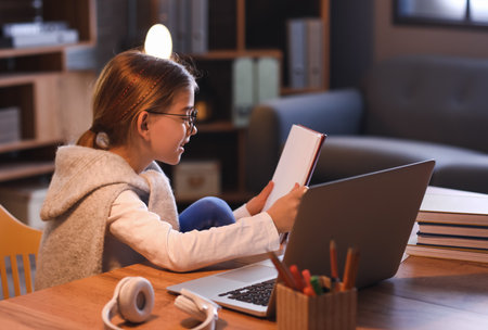 Little girl studying online at home in the evening