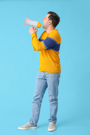 Protesting young man with megaphone on color backgroundの写真素材