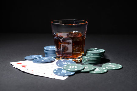 Poker chips, glass of beverage and cards on dark background