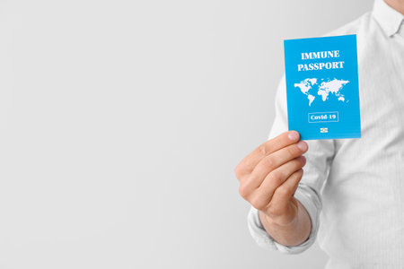 Young man with immune passport on gray backgroundの写真素材
