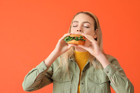 Young woman eating tasty vegan burger on color backgroundの写真素材