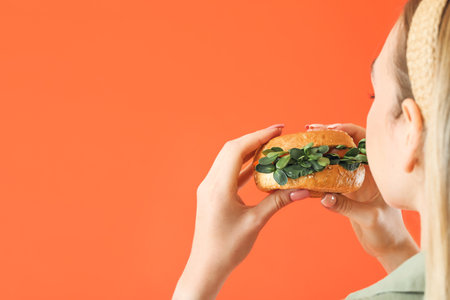Young woman eating tasty vegan burger on color backgroundの写真素材