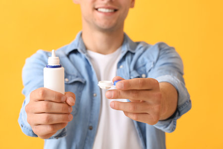 Young man with contact lenses and bottle of solution on color background, closeupの写真素材