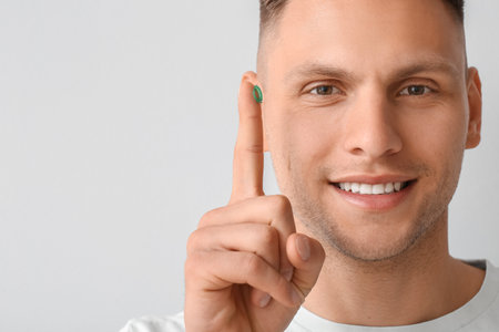 Young man putting in contact lens on light backgroundの写真素材