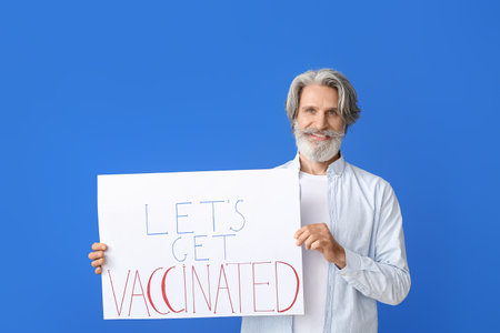 Senior man holding poster with text LET'S GET VACCINATED on color backgroundの写真素材