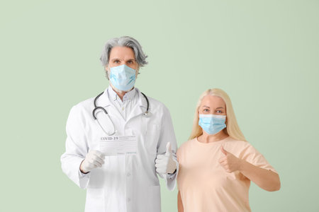 Doctor and patient with International Certificate of Vaccination showing thumb-up on color backgroundの写真素材