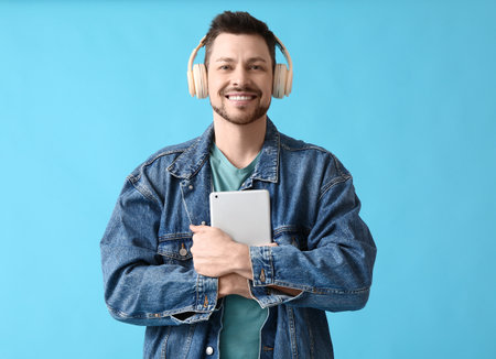 Man with tablet computer and headphones on color background