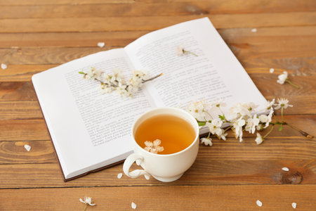 Cup with tasty tea, book and blooming branches on wooden backgroundの写真素材