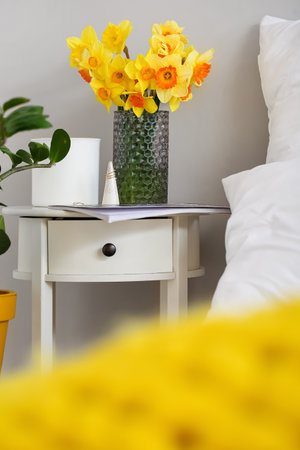 Vase with narcissus flowers on bedside table in roomの写真素材