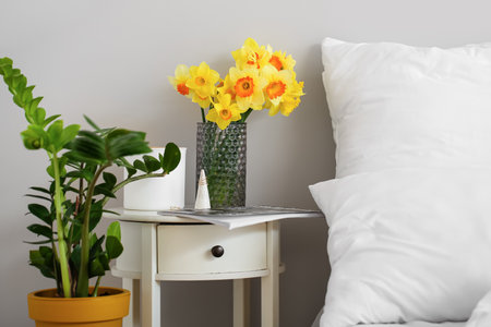 Vase with narcissus flowers on bedside table in roomの写真素材