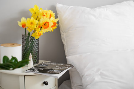 Vase with narcissus flowers on bedside table in roomの写真素材