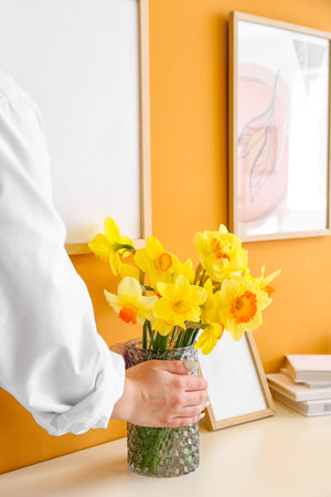 Woman with beautiful bouquet of narcissus flowers in roomの写真素材
